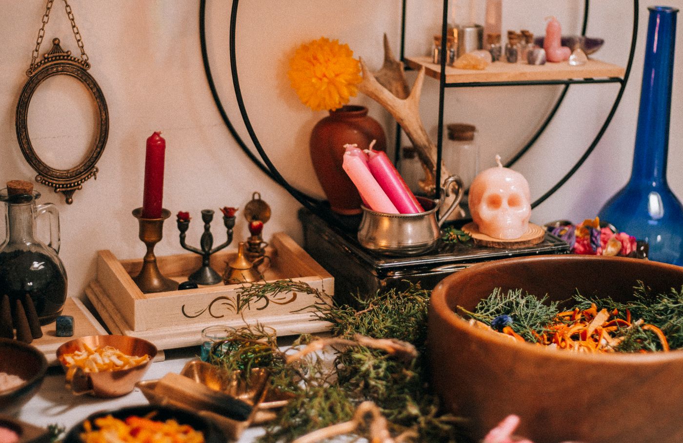 A dark green altar with candles, dried herbs, bottles, and crystals