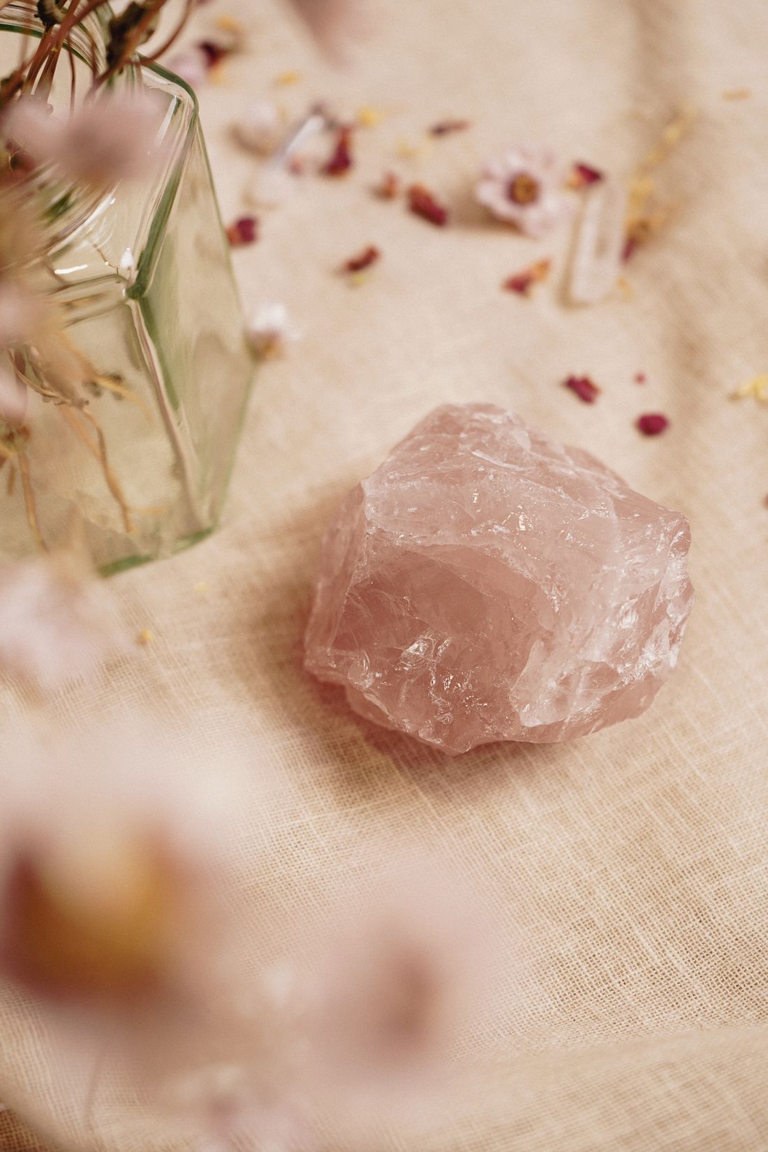 A natural rose quartz stone beside dried flower petals